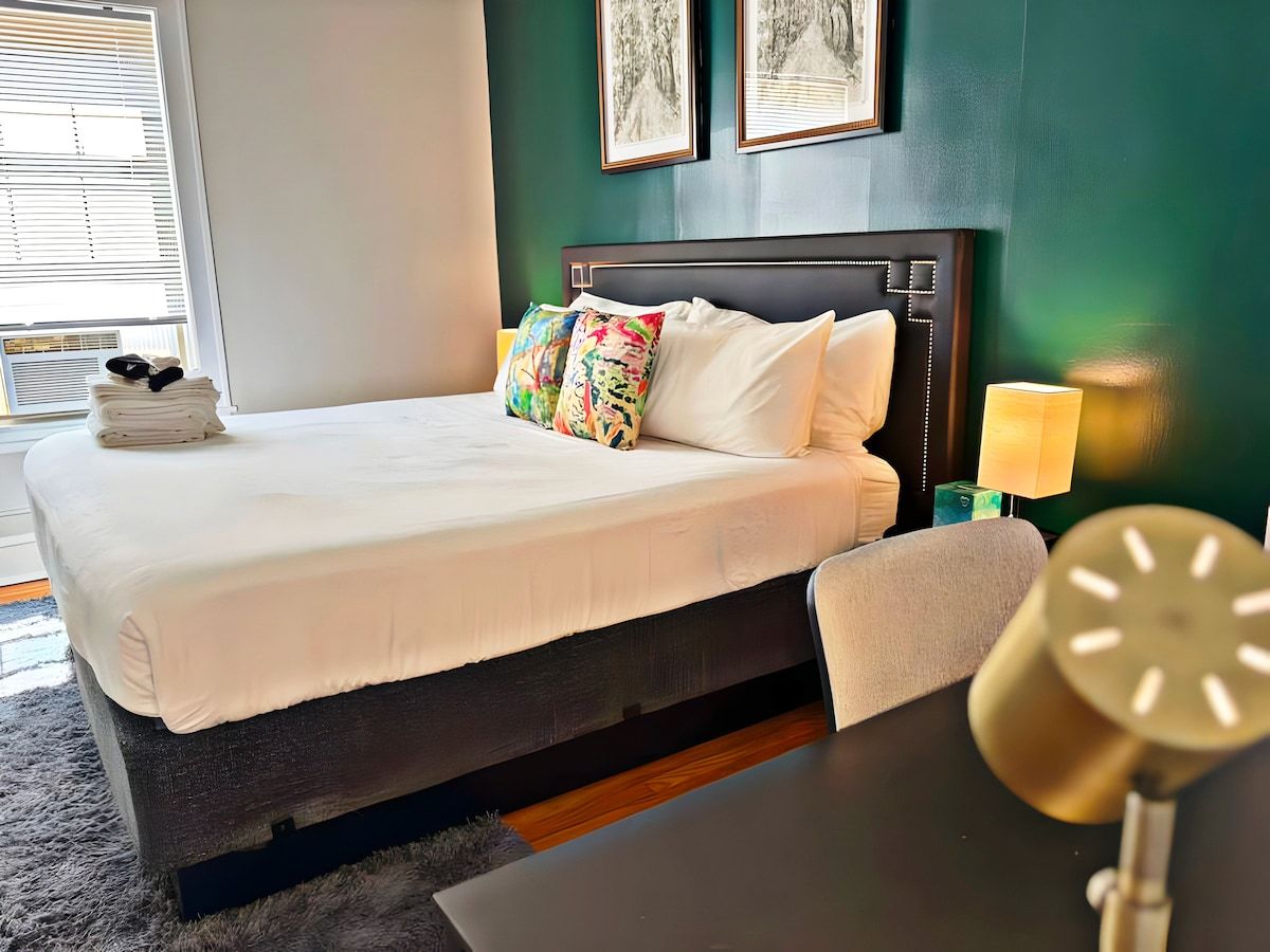Una habitación de hotel con una cama, una silla, una mesita de noche y una lámpara.