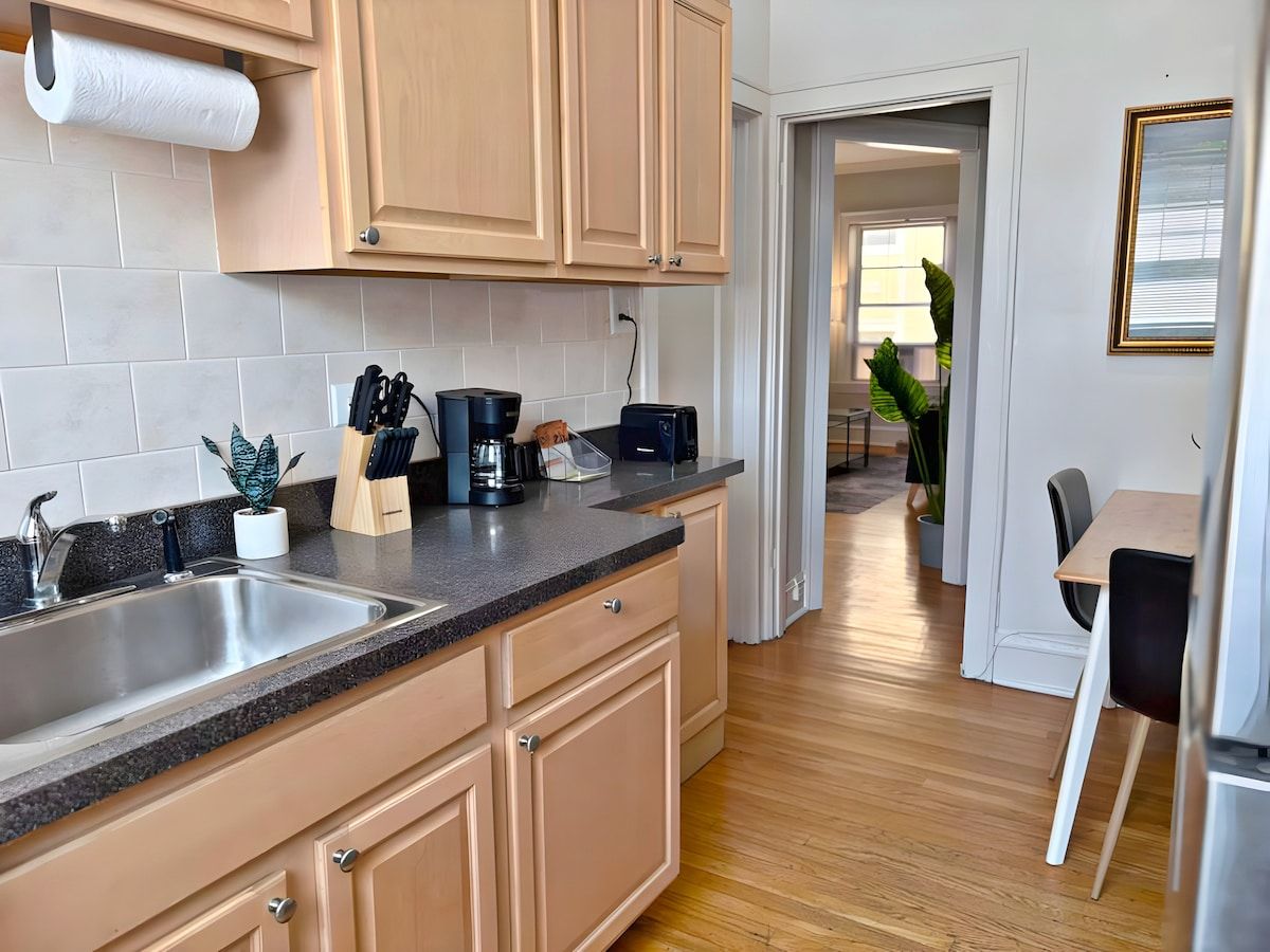 A modern kitchen with wooden cabinets, a granite countertop, and a dining area with a table and chairs.