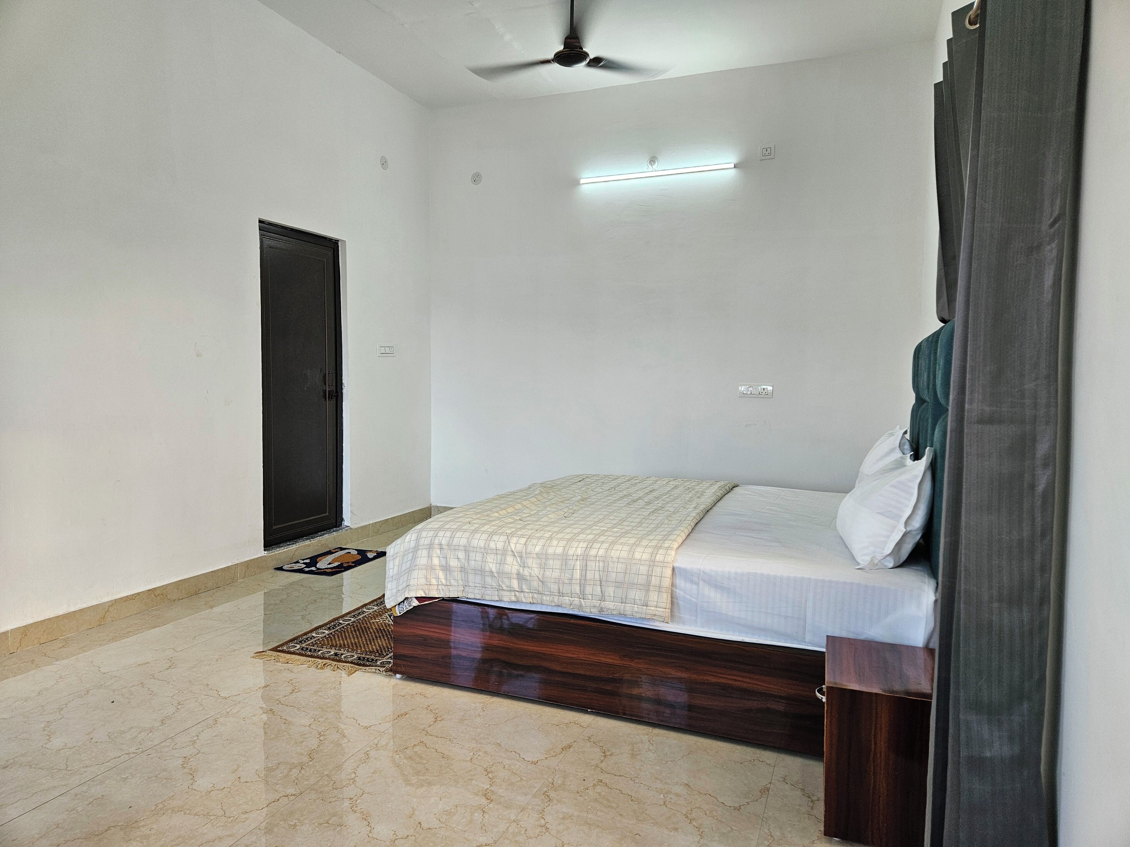 A bedroom with a bed, a ceiling fan, a light fixture, and a door.