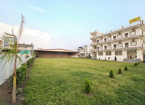 A hotel with a flat roof, multiple balconies, and a well-maintained lawn. - Hotel YesWell (Rishikesh)