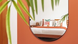 Un dormitorio con cama, almohadas, una mesita de noche y un espejo que refleja la habitación.