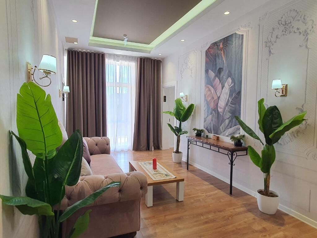 Una sala de estar con sofá, mesa de centro, plantas en macetas y un cuadro en la pared.