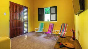 A room with a wooden door, a window with shutters, and three colorful chairs. - Casa Amarela em Icaraí de Amontada (Amontada)