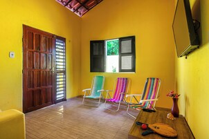 Um quarto com porta de madeira, janela com persianas e três cadeiras coloridas.