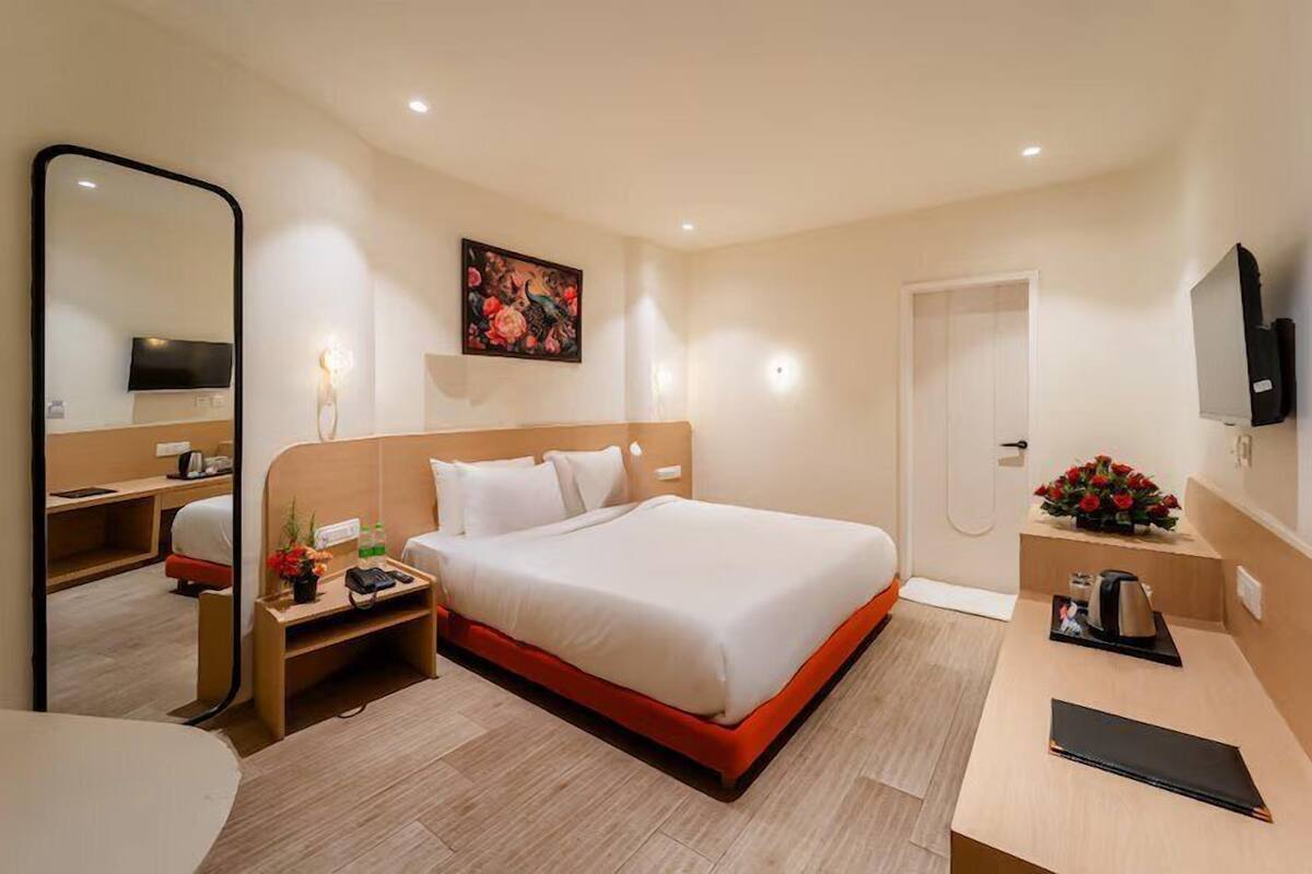 Ein Hotelzimmer mit Bett, Nachttisch, Spiegel, Kunstwerk, Fernseher und Schreibtisch mit Wasserkocher.