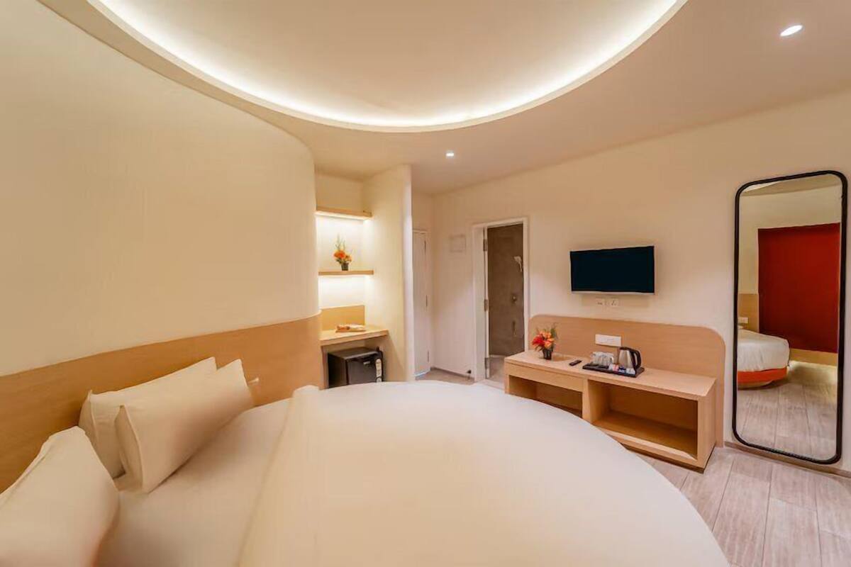 Ein modernes Hotelzimmer mit einem großen Bett, einem Nachttisch, einem Fernseher und einem Spiegel.