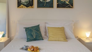 A neatly made bed with a tray of pastries and a cup, two pillows with distinct patterns, and three framed artworks above the bed. - Elegant 2 Suites Residence,city centre,near Famous Castrocaro Thermal Baths (Castrocaro Terme)