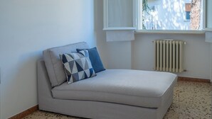 A corner room with a grey sofa, a patterned pillow, a radiator, and a window with a view of trees. - Elegant 2 Suites Residence,city centre,near Famous Castrocaro Thermal Baths (Castrocaro Terme)