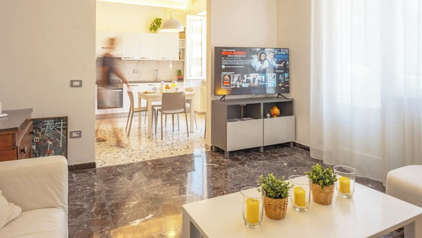 A modern living room with a flat-screen TV, a dining area with chairs, and a kitchen in the background. - Elegant 2 Suites Residence,city centre,near Famous Castrocaro Thermal Baths (Castrocaro Terme)
