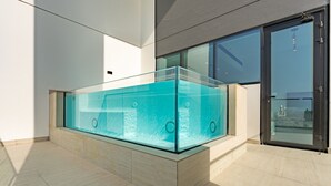 Une piscine intérieure moderne aux parois en verre transparent, située dans une pièce spacieuse dotée d’un sol carrelé et de grandes fenêtres.