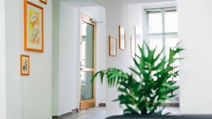 Een gang met ingelijste kunstwerken aan de muren, een deur naar een andere kamer, en een plant in pot voorop.
