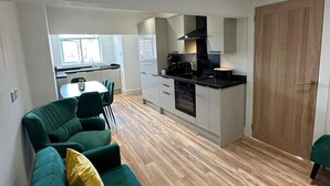 A compact kitchen with modern appliances, a dining area with green chairs, and a wooden floor. - 6 Guests/free Parking/old Trafford/20min City (Manchester)