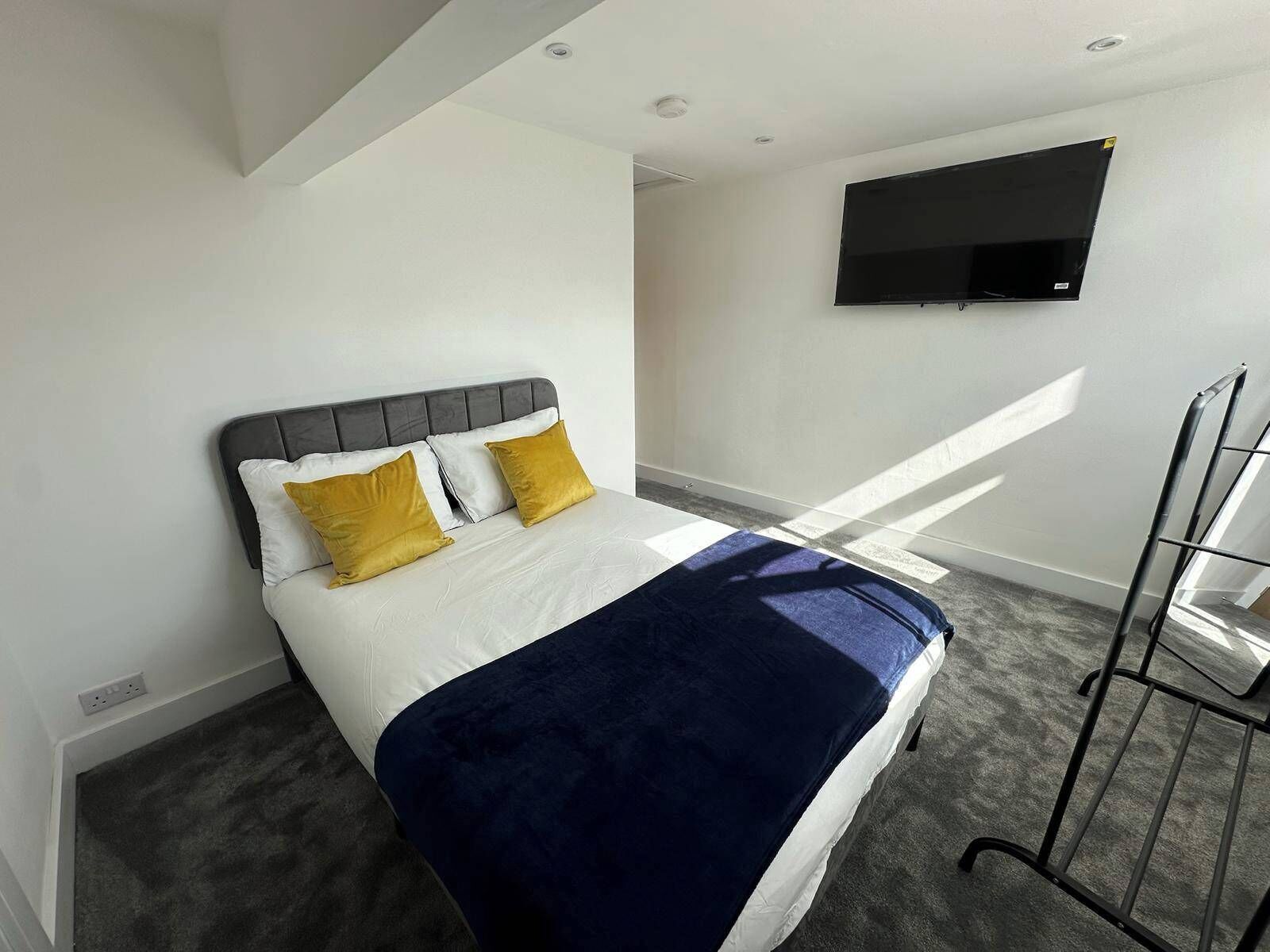 A modern hotel room with a bed, a flat-screen TV mounted on the wall, and a window providing natural light.