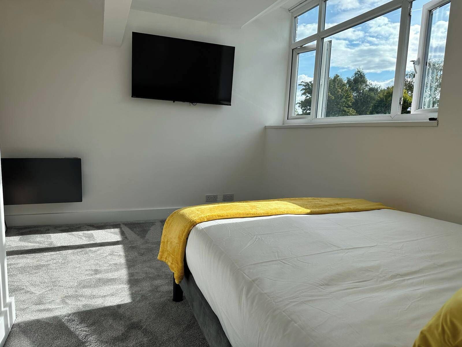 Een slaapkamer met een bed, een flatscreen televisie aan de muur en een raam met uitzicht op bomen.