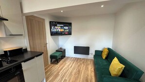 A compact living space with a kitchenette, a green sofa with yellow pillows, and a flat-screen TV mounted on the wall. - 6 Guests/free Parking/old Trafford/20min City (Manchester)