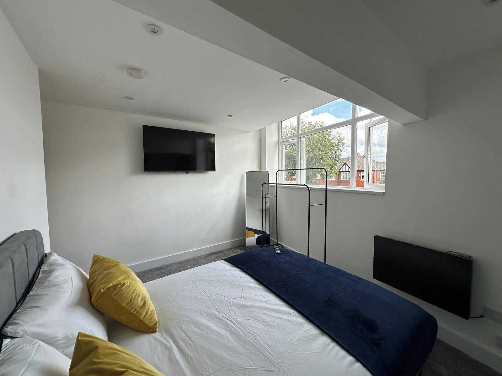 A modern hotel room with a bed, a TV mounted on the wall, and a window providing a view of the outside.