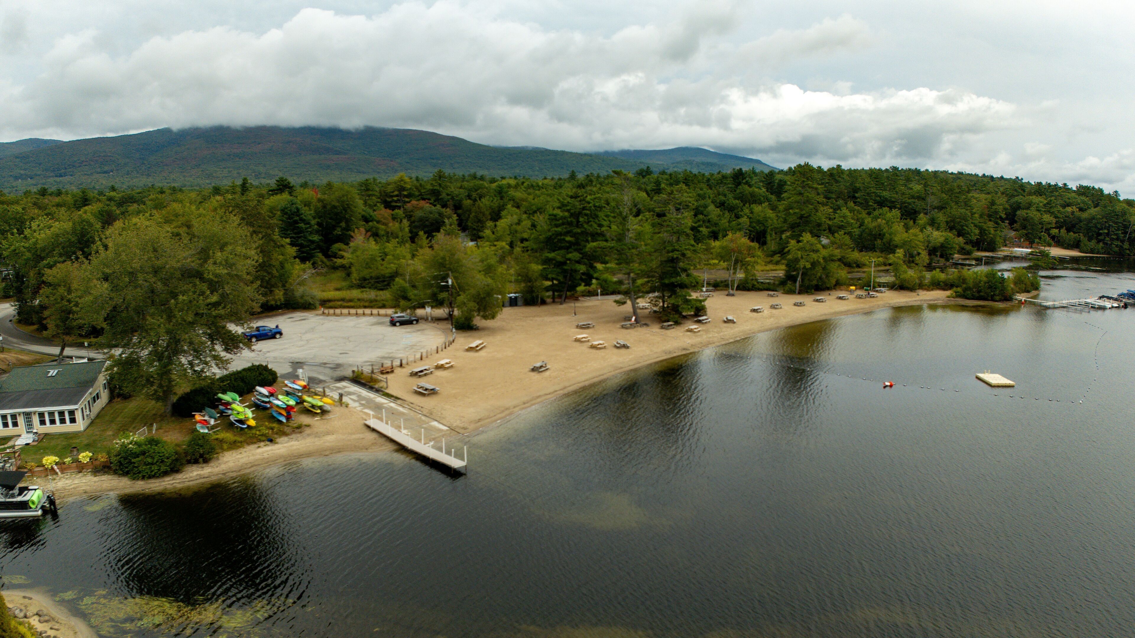 Vue aérienne d’une zone au bord d’un lac, avec un parking, des bateaux et un quai.