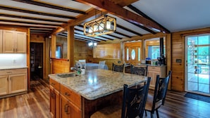 Interior de una cabaña de madera con una cocina que incluye una encimera de granito, armarios de madera y una mesa de comedor con sillas.