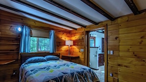 Dormitorio de cabaña de madera con una cama, una mesita de noche, una lámpara y un ventanal con cortinas.