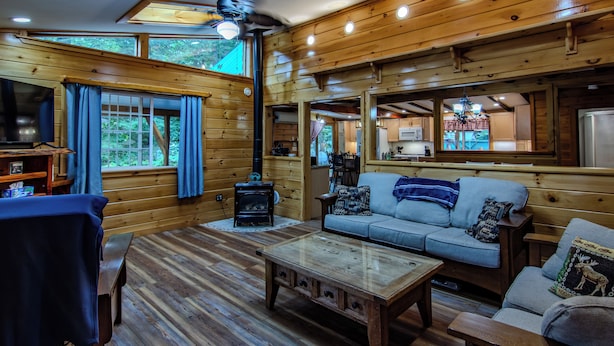 Interior acogedor de una cabaña con piso de madera, un sofá, una mesa de centro y una chimenea.