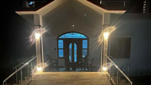 A building with a covered entrance, a staircase leading up to it, and a lit blue sign above the door. - Wilder Lust Homestay (Bhira)