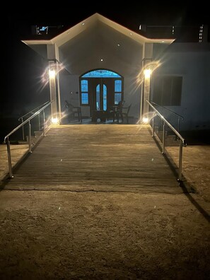 A building with a covered entrance, a staircase leading up to it, and a lit blue sign above the door.