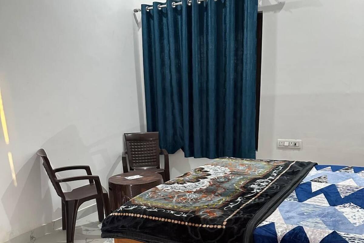A bedroom with a wooden bed, a patterned quilt, a dark blue curtain, a small round table, and a chair.