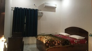A bedroom with a bed, a desk, a chair, a window with curtains, an air conditioner, and a ceiling fan. - Wilder Lust Homestay (Bhira)