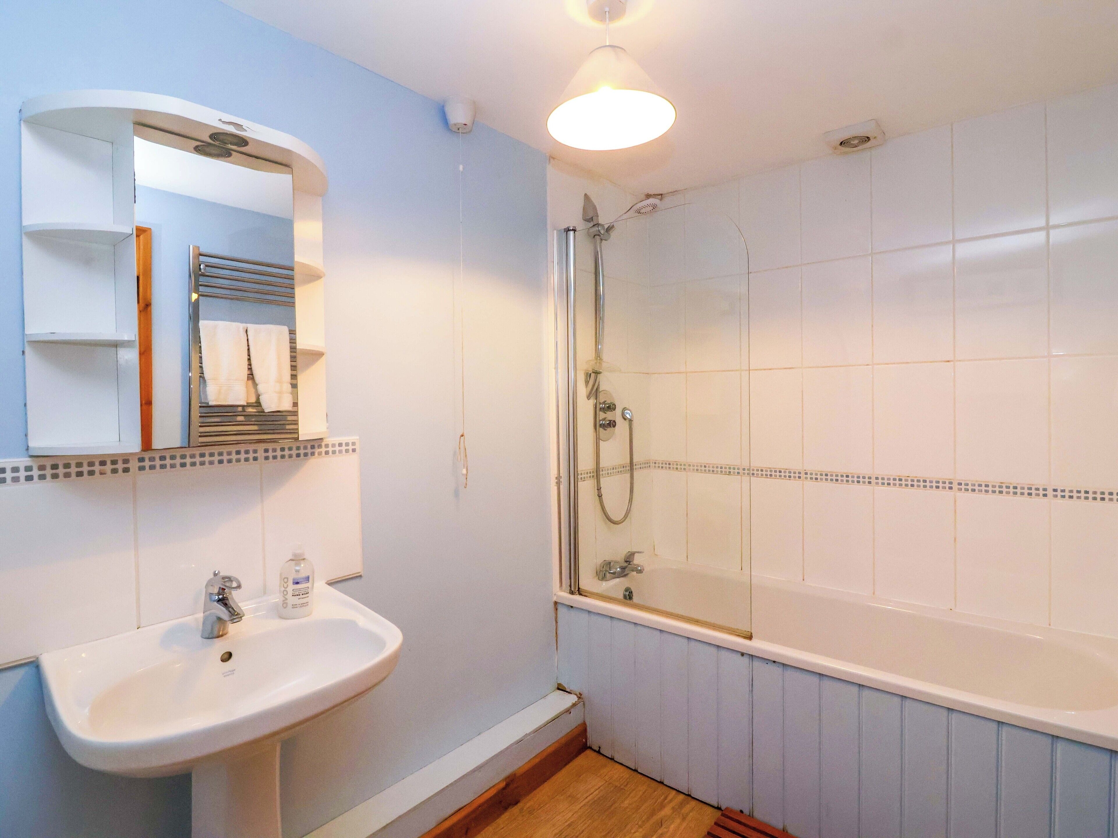A bathroom with a white sink, a mirror, a shower with a glass door, and a tiled floor.