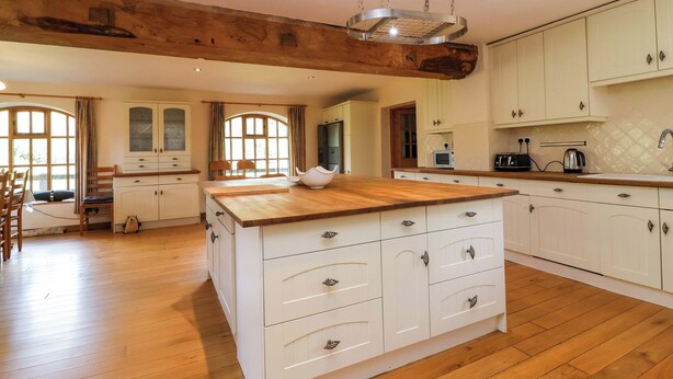 A spacious kitchen with wooden flooring, white cabinetry, and a central island. - Millbarn (Taunton)