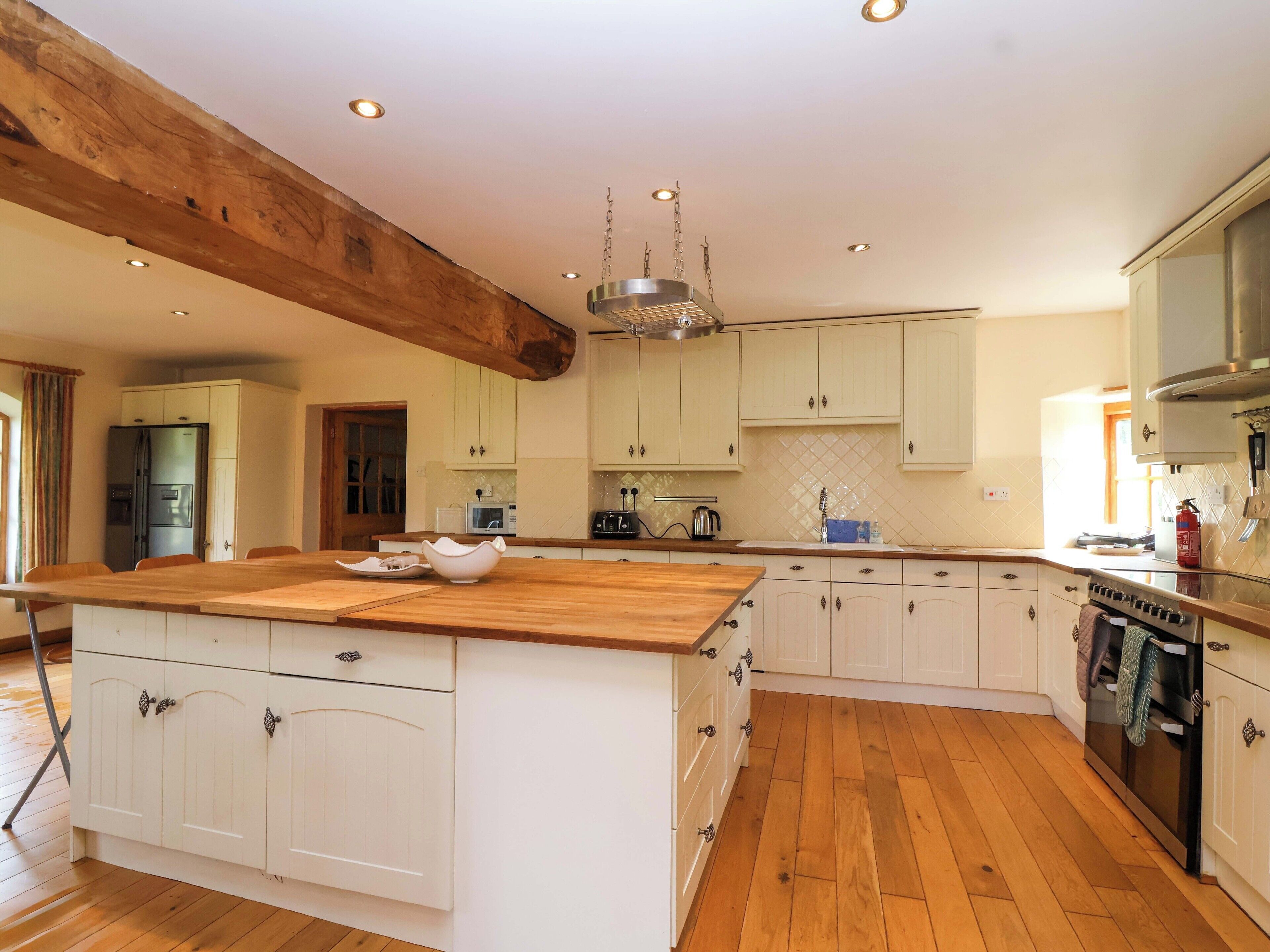 A spacious kitchen with wooden flooring, white cabinetry, a central island, and a hanging light fixture.