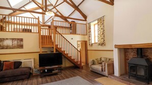 A spacious living room with a wooden staircase, a fireplace, a television, and a cozy sofa. - Millbarn (Taunton)