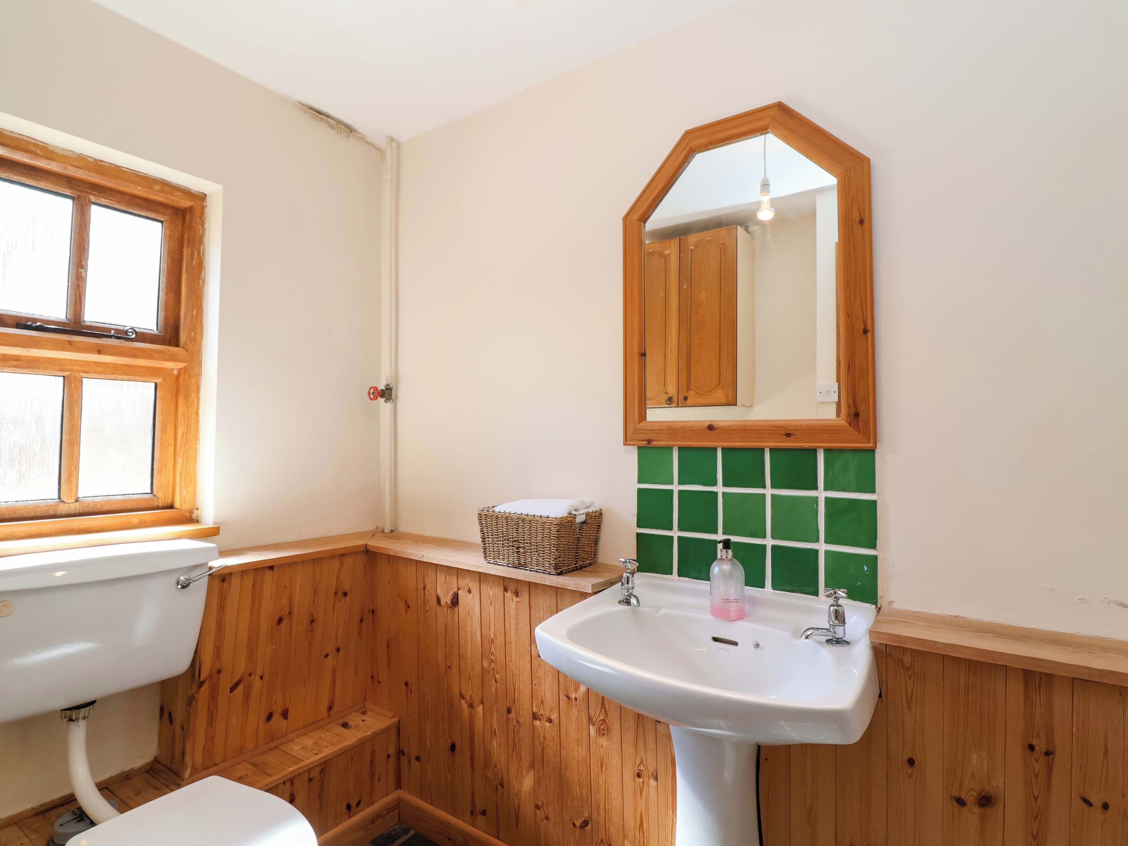 A bathroom with a wooden floor, a white sink, a mirror, and a window.