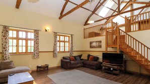 A spacious living room with wooden flooring, a large sectional sofa, a coffee table, and a staircase leading to an upper level. - Millbarn (Taunton)