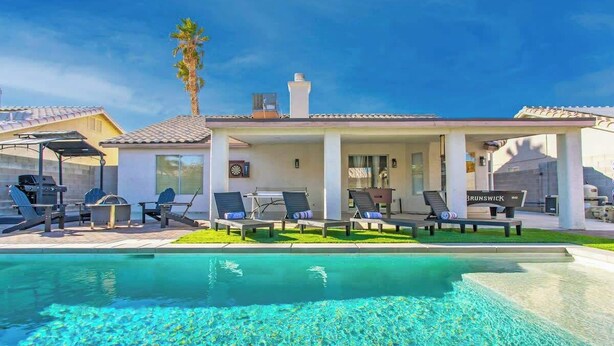 Un espace aménagé au bord de la piscine, avec des chaises longues, un barbecue et une terrasse couverte.