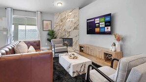 Un salon moderne avec un canapé en cuir, une table basse en marbre, un téléviseur fixé au mur diffusant des services de streaming et une cheminée.
