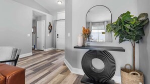 Un couloir moderne avec un plancher en bois, une console noire agrémentée d’un miroir et une grande plante en pot.