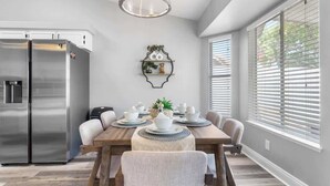 Une cuisine moderne avec un réfrigérateur en acier inoxydable, une table à manger dressée avec des assiettes et des bols blancs, et un luminaire suspendu au-dessus.