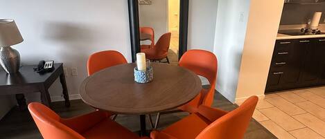 Un espace repas moderne avec une table ronde et des chaises orange, un miroir au mur et une cuisine dotée de meubles sombres.