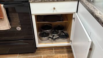 A kitchen with a black stove, a wooden countertop, a white cabinet, and a drawer with pots.