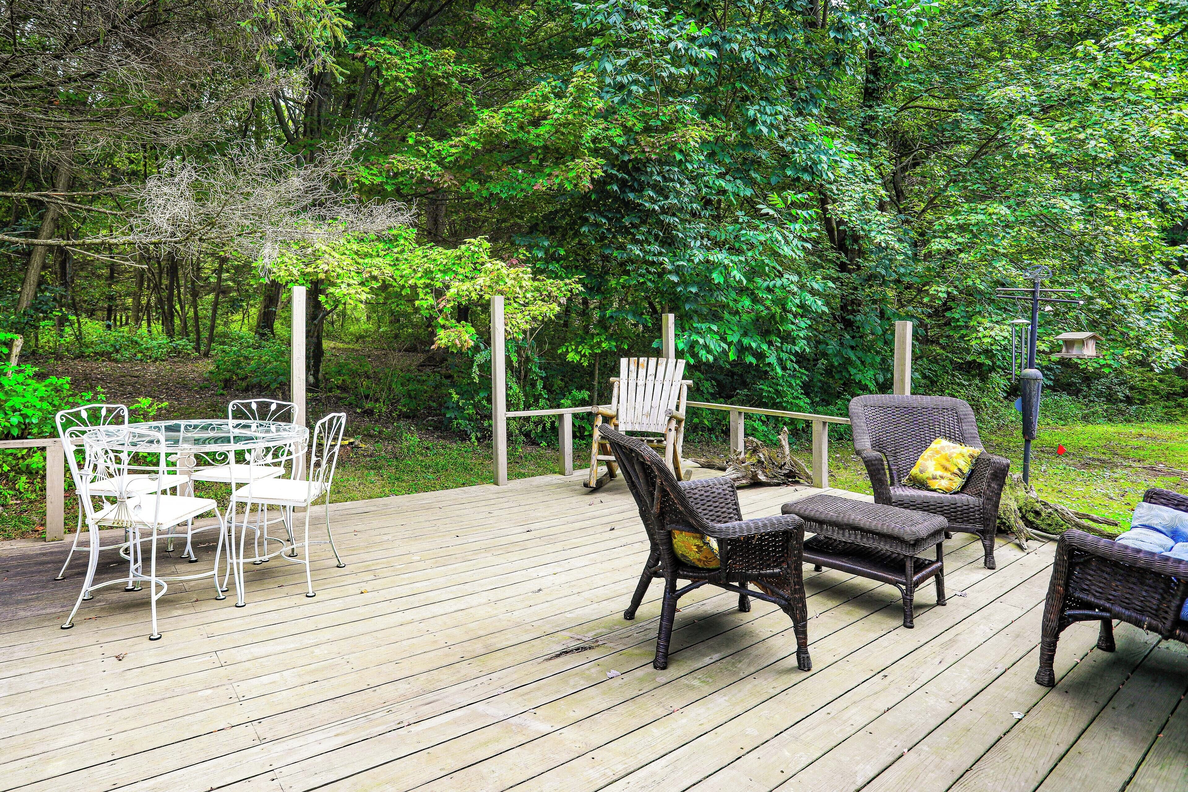 A wooden deck with outdoor furniture, including a table and chairs, surrounded by lush greenery.