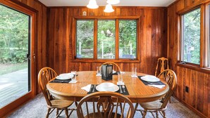 A wooden-paneled dining room with a large window, a chandelier, and a table set for six.