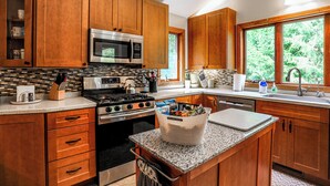 A kitchen with wooden cabinets, stainless steel appliances, a granite countertop, and a window providing a view of greenery.