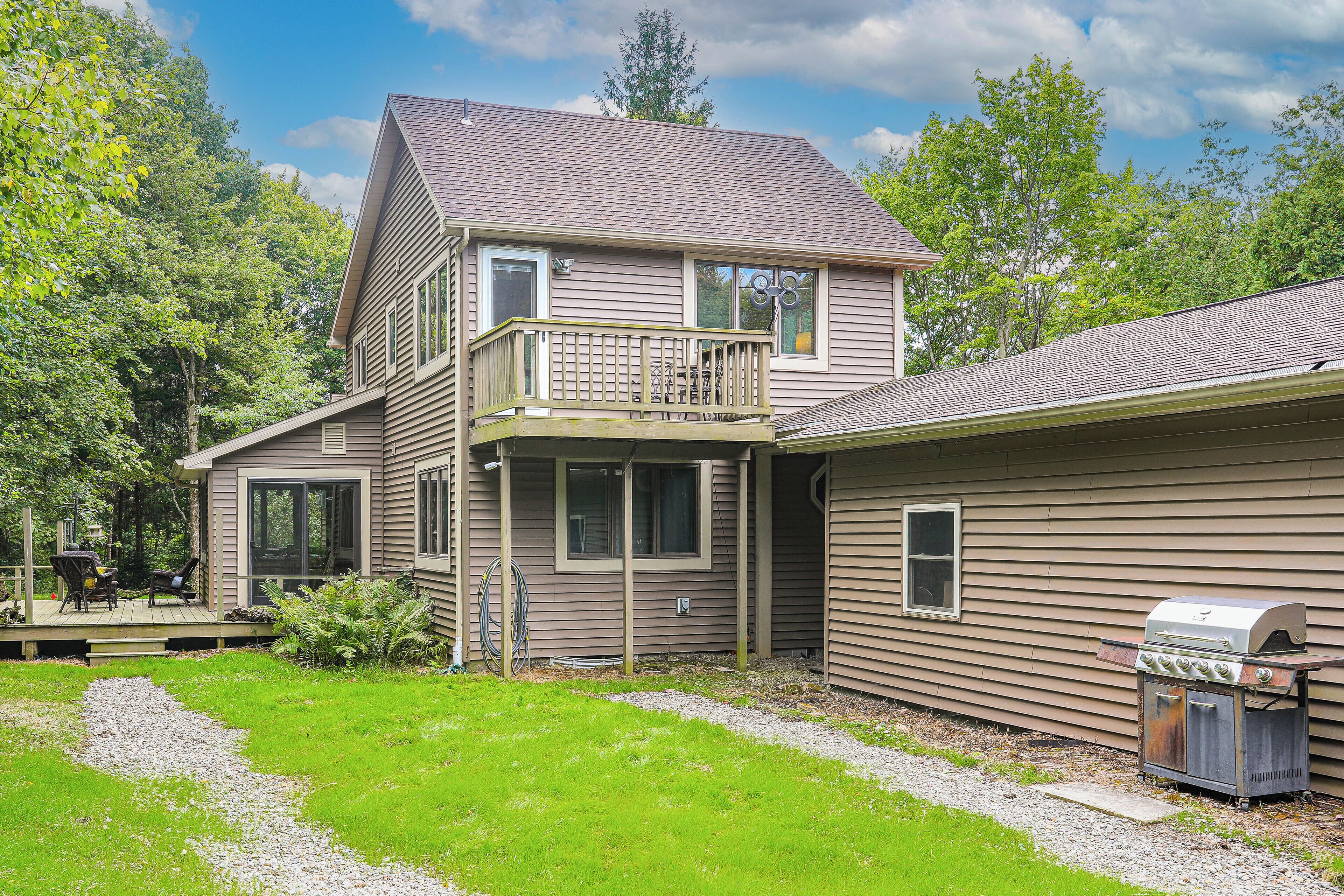 A two-story house with a deck, a barbecue grill, and a large window.