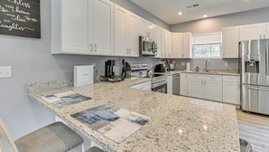 Una cocina moderna con armarios blancos, encimeras de granito, electrodomésticos de acero inoxidable y un salpicadero con un diseño de mosaicos decorativos.