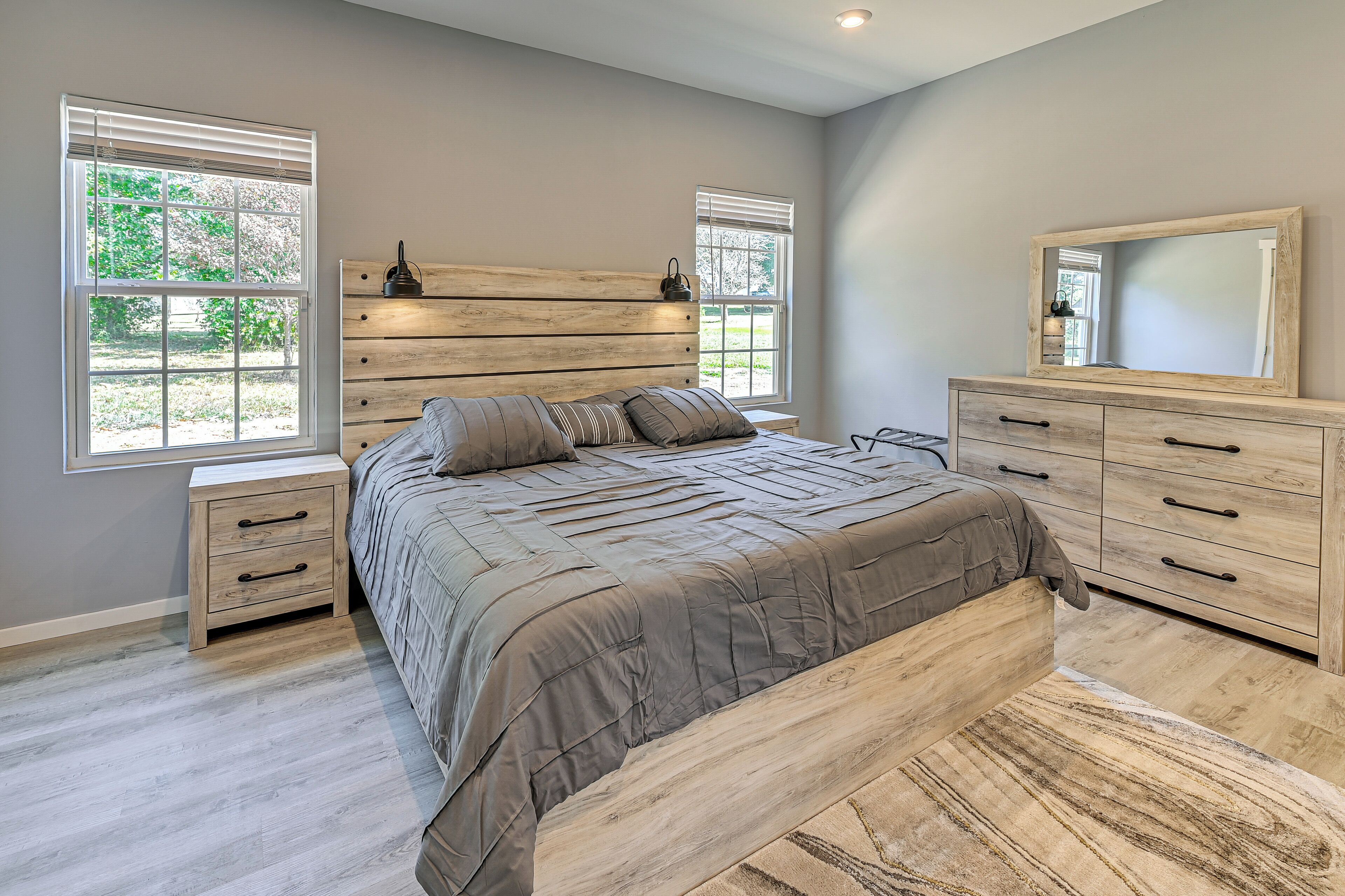 A bedroom with a large bed, wooden headboard, two bedside tables, a dresser, and a mirror.