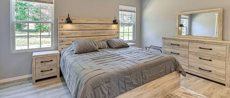 A bedroom with a large bed, wooden headboard, two bedside tables, a dresser, and a mirror.