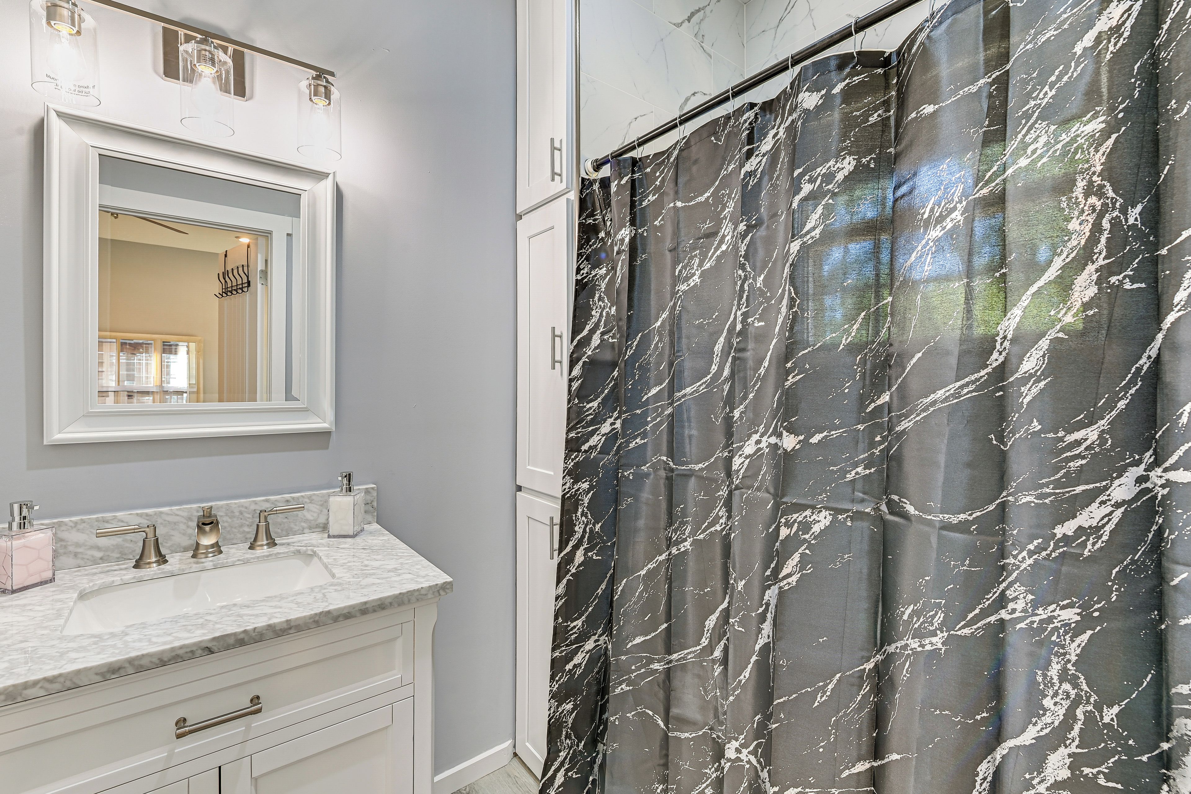 A bathroom with a marble sink, a mirror, and a shower curtain with a marble pattern.