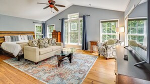 A spacious living room with a high ceiling, a ceiling fan, a large window with curtains, a sofa set, a coffee table, and a television. - 30 Acres & Pond: North Georgia Mtn Farmhouse (Demorest)
