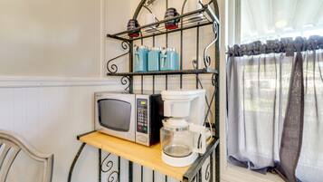 A kitchen area with a microwave, coffee maker, and a shelf with cups.